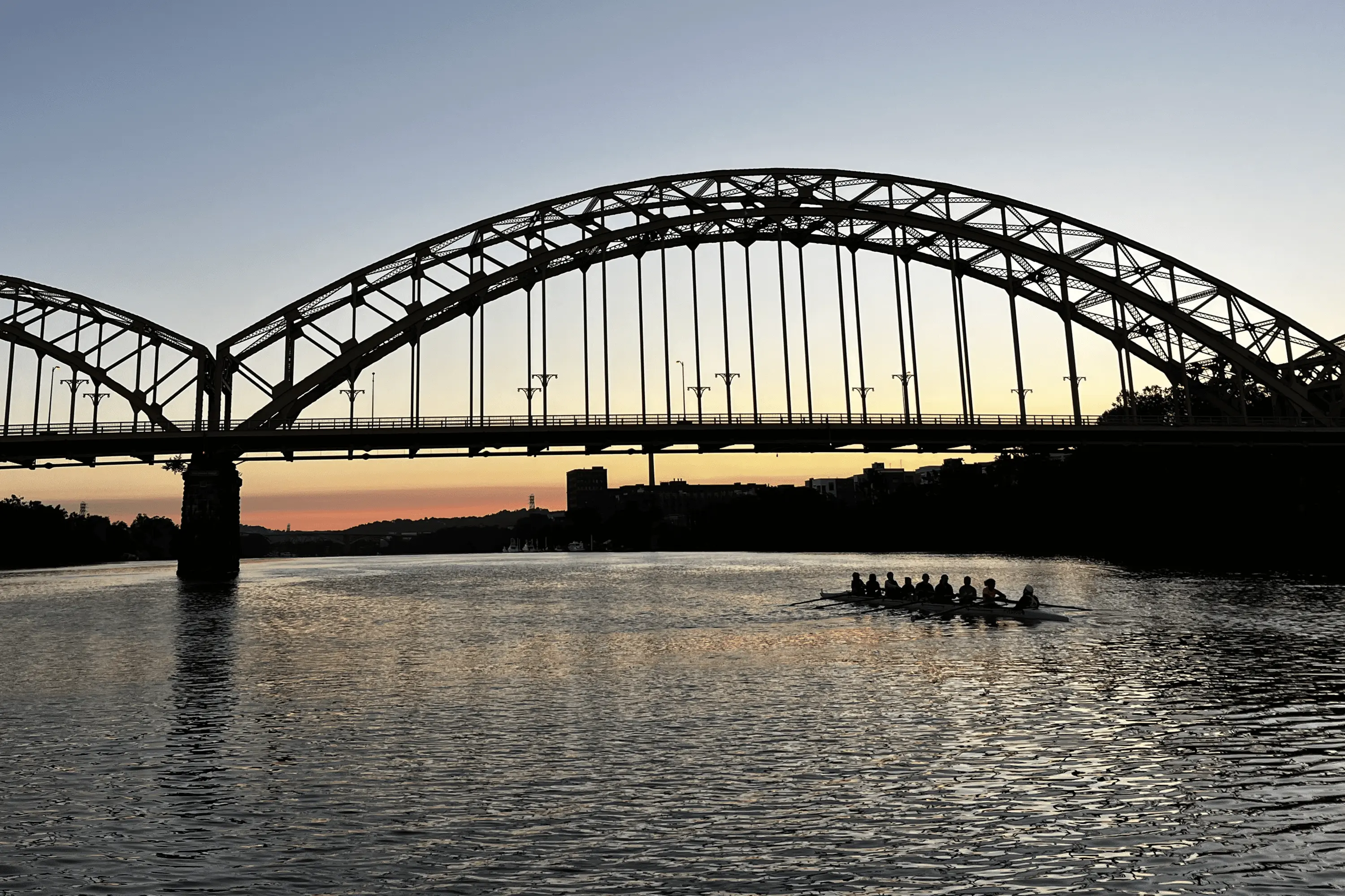 A rowing team in the Allegheny River during sunset